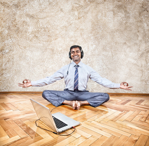 Business yoga (Indian businessman listening to the music with headphones and doing meditation near the laptop in the office)